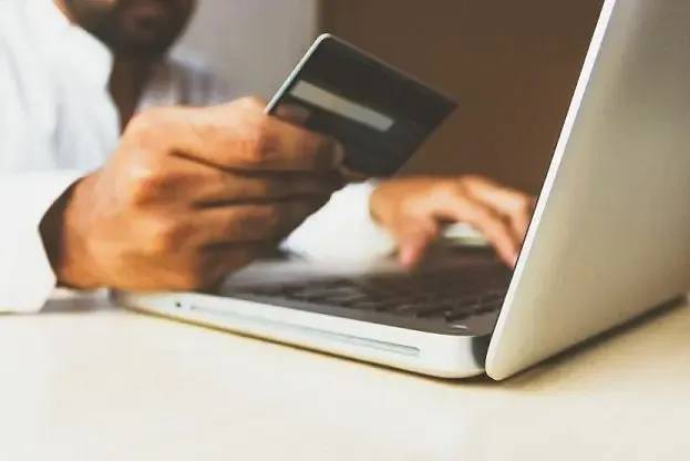 Person holding a credit card and using a laptop to buy a premium domain name online.