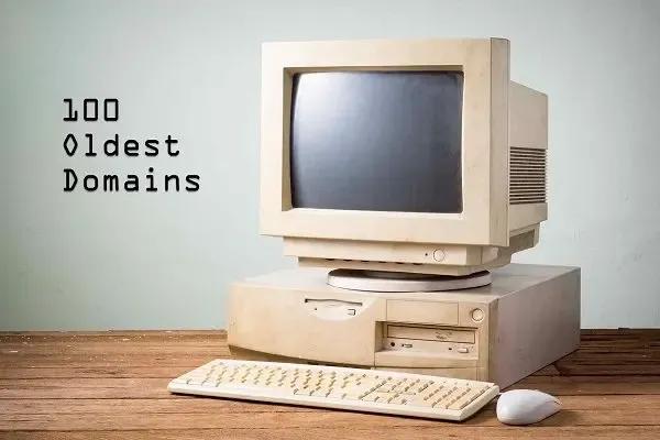 Vintage computer with keyboard and mouse on wooden desk, with text ‘100 Oldest Domains’ — representing the first registered domain names on the internet.